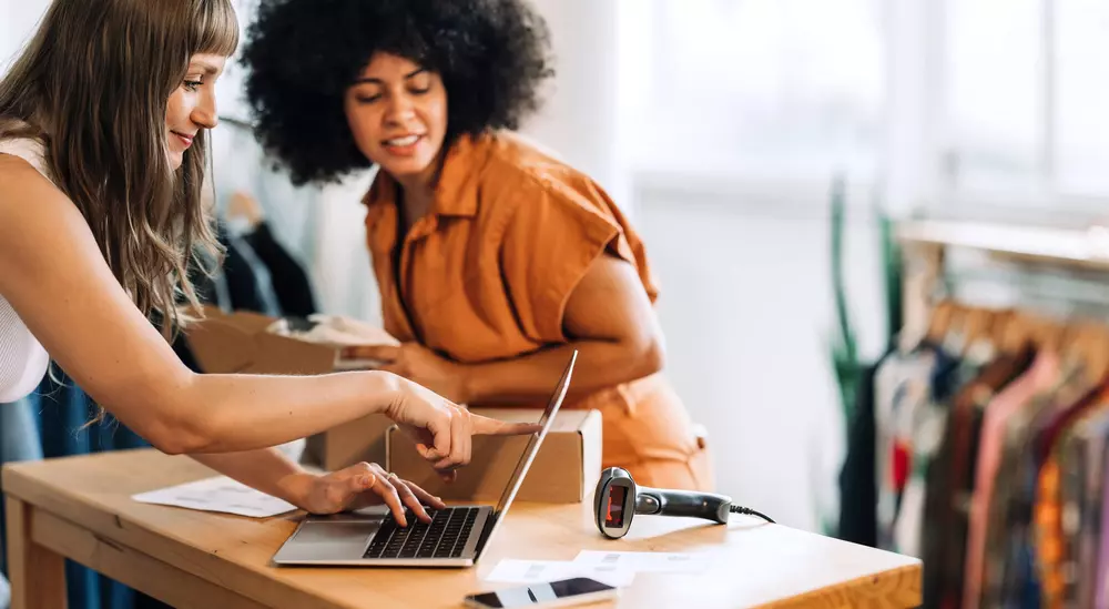 Two women in warehouse using laptop